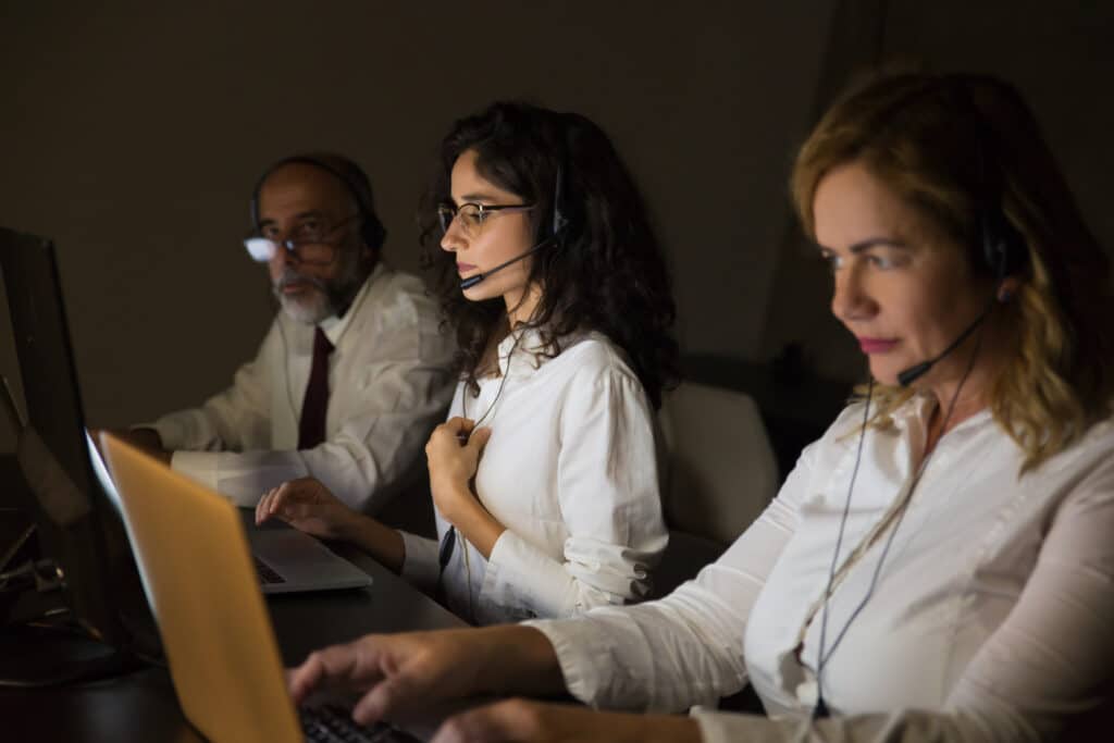 Profissionais de call center atendendo clientes com headsets em ambiente corporativo.