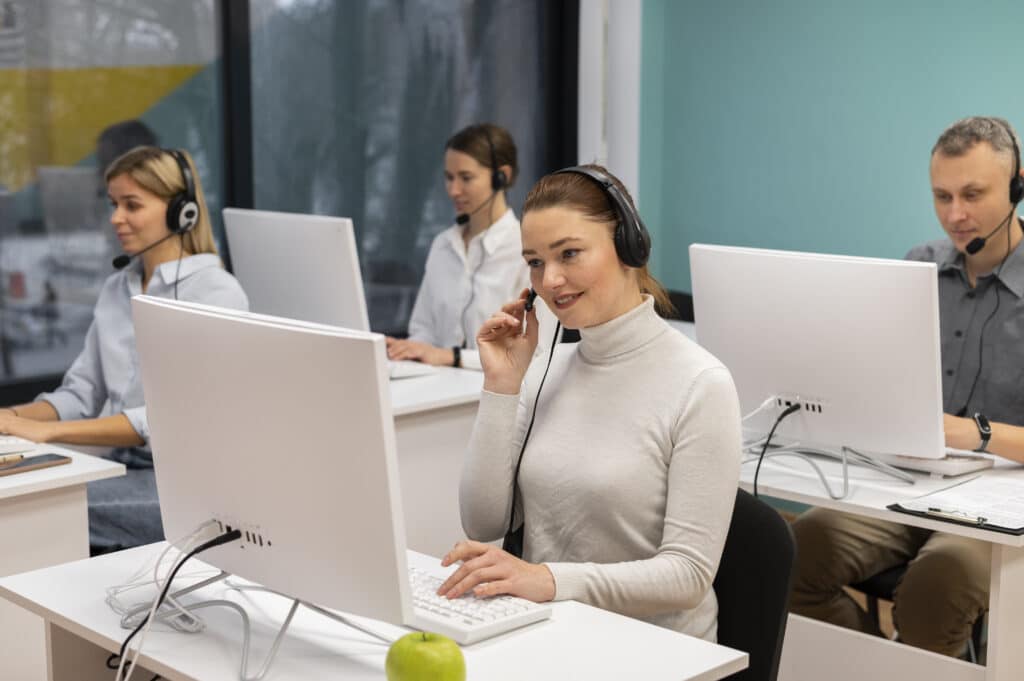 Equipe de atendimento em call center usando headsets e computadores em escritório moderno.