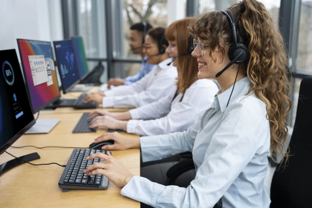 Equipe de call center usando headsets e computadores em linha; foco em atendente sorridente ao teclado.