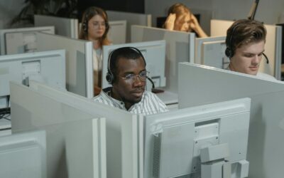 Operação de call center com agentes em atendimento Operadores de call center utilizando headsets em estação de atendimento com computadores e divisórias.