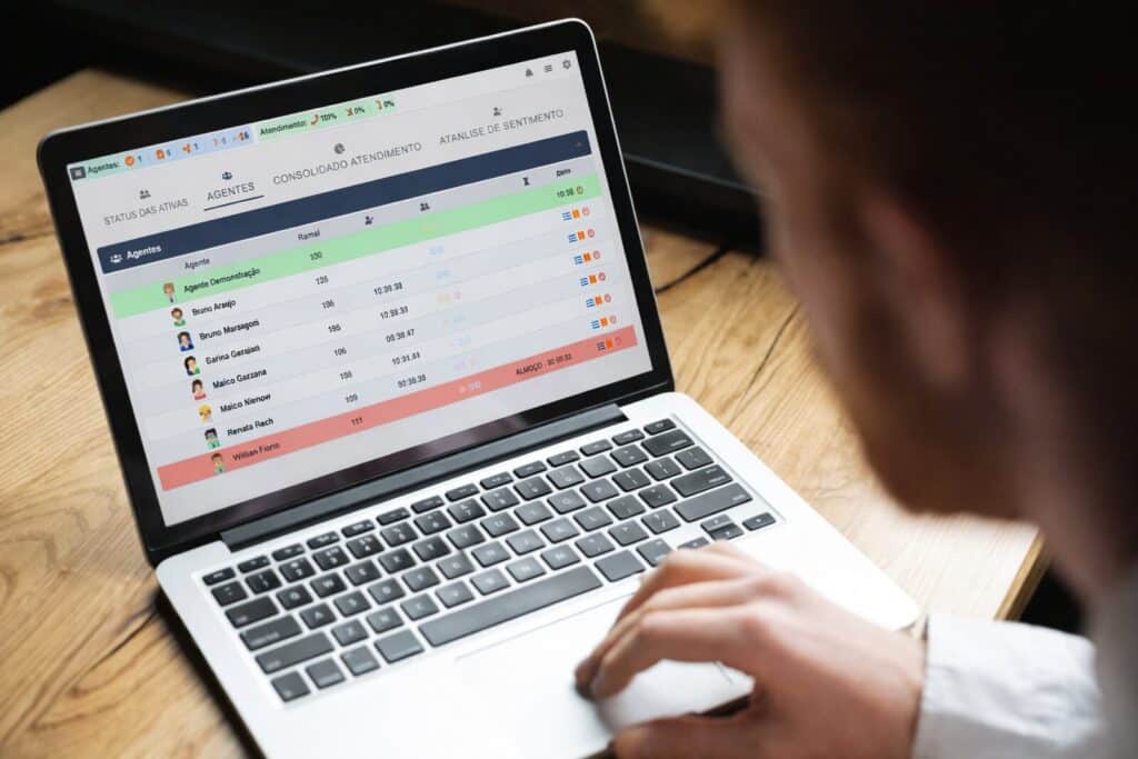 Dashboard de atendimento sendo monitorado em laptop com indicadores de agentes e filas de call center